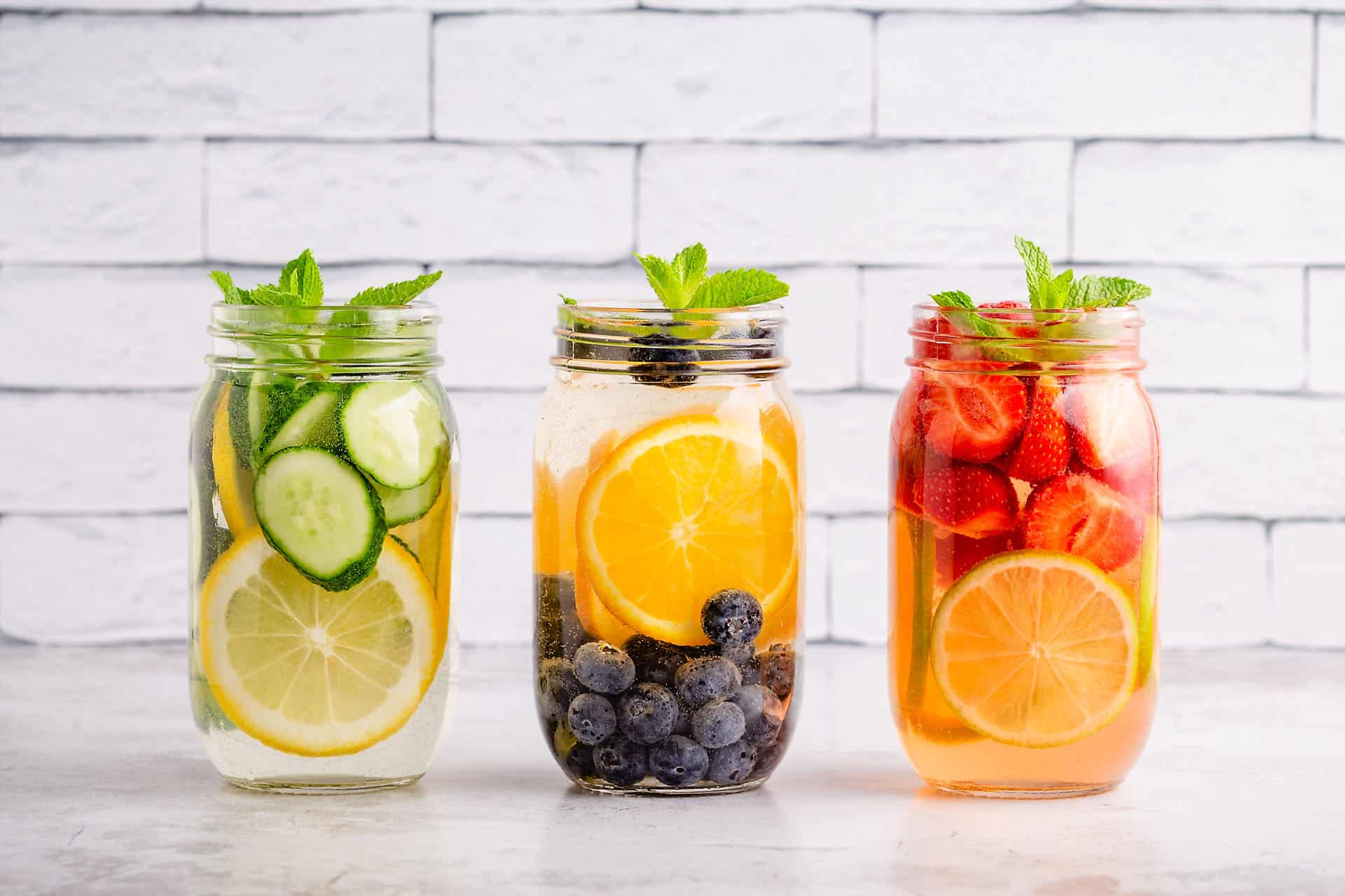 Three jars of fruit infused water with fresh citrus and berries, promoting healthy hydration and heart healthy lifestyle choices.