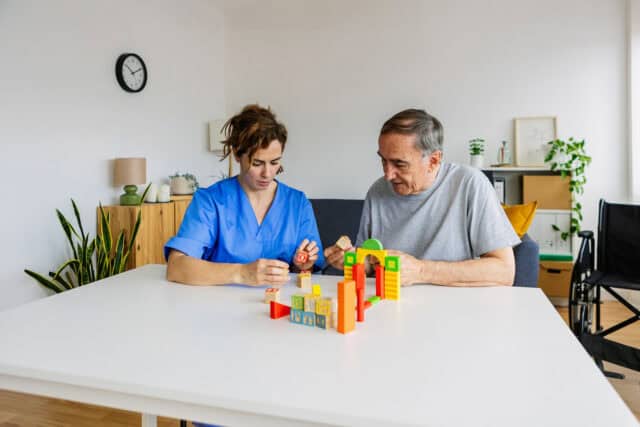 Occupational therapist helping an adult improve fine motor skills and hand coordination using building blocks during a therapy session.