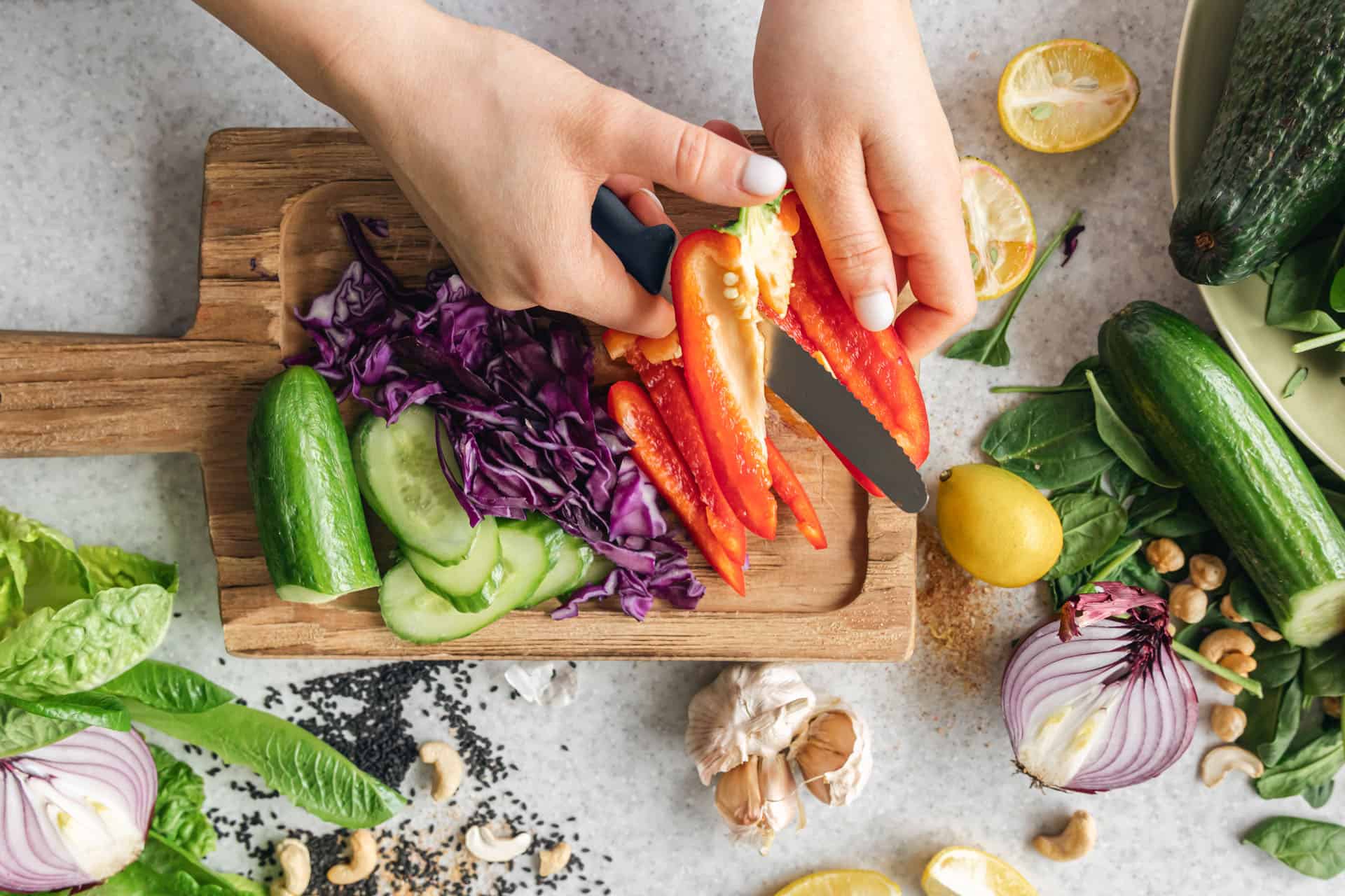 Hands preparing fresh vegetables on a cutting board as part of healthy meal planning and nutritional behavior modification.