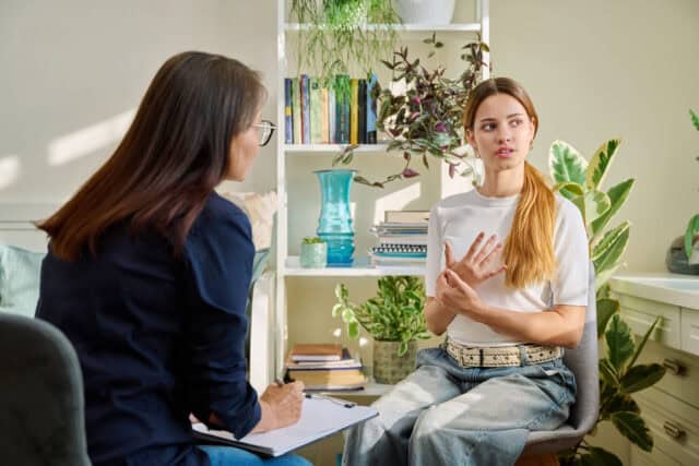 A therapist listens attentively as a young woman shares her thoughts during a psychological counseling session.