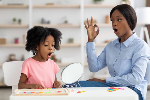 Speech therapist working with a child using a mirror and articulation exercises to improve speech and communication skills.