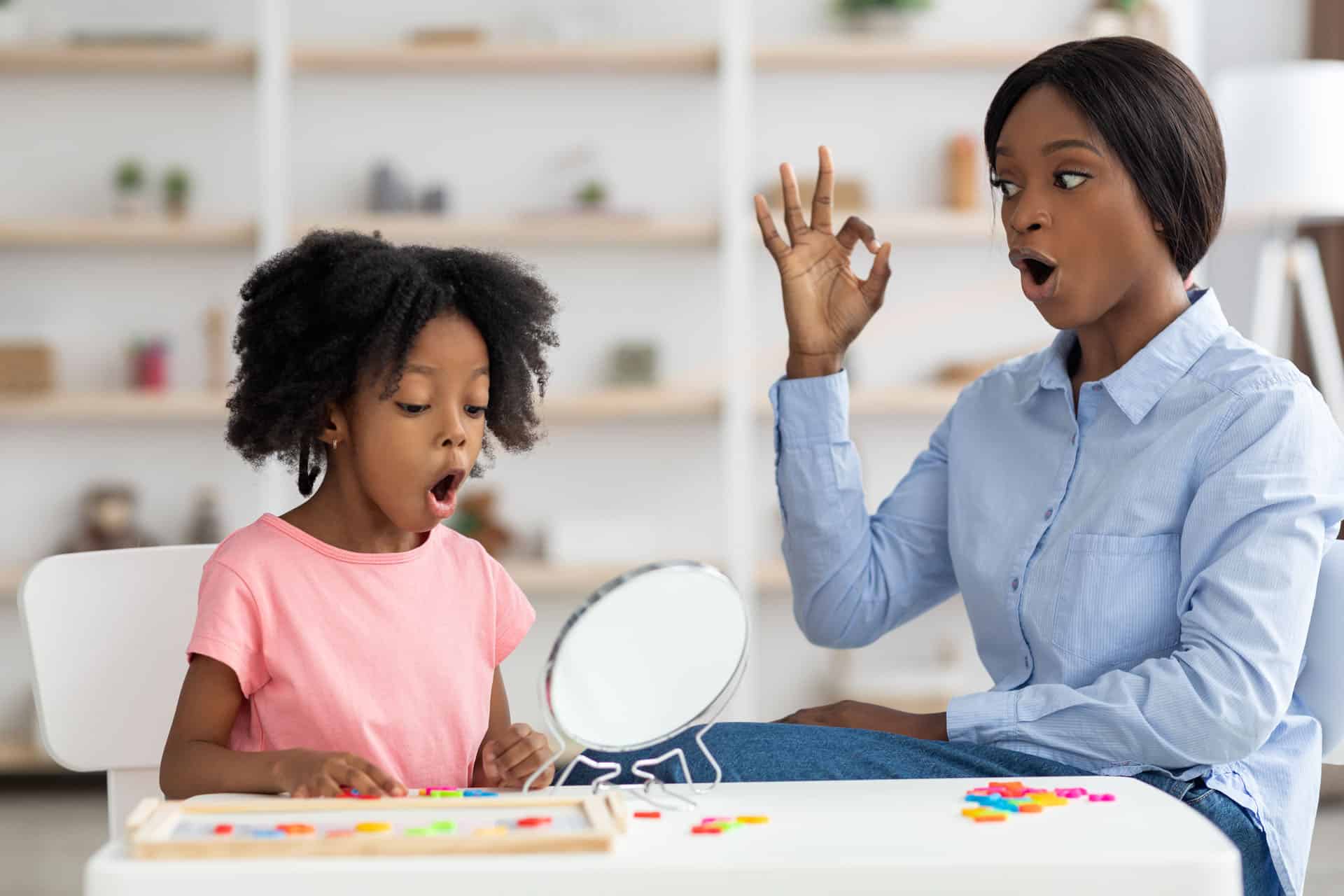 Speech therapist working with a child using a mirror and articulation exercises to improve speech and communication skills.