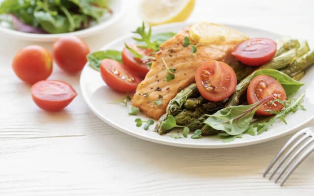 heart healthy eating habits illustrated by a meal of cooked salmon, asparagus, cherry tomatoes and leafy greens all of which form part of heart health nutrition.